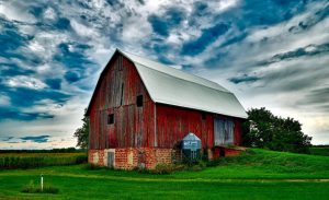 A red barn on a large patch of green grass under a blue sky.