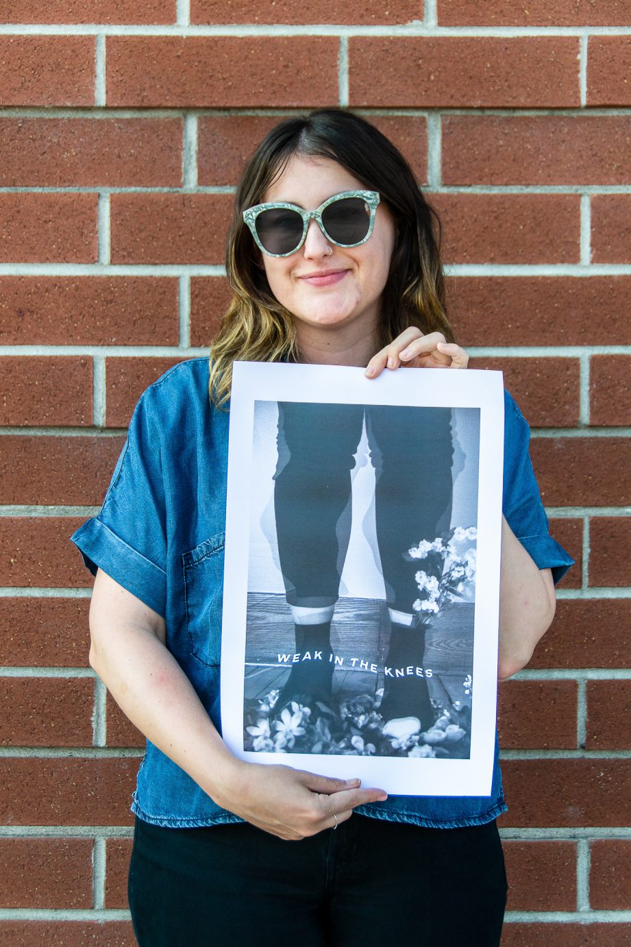 Ashley King holds a piece of her art in front a red-brick building.