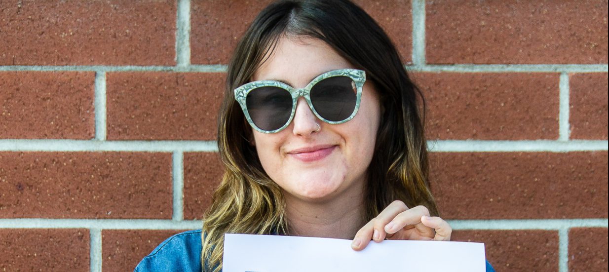 Ashley King hold a piece of her art in front of a red-brick building.