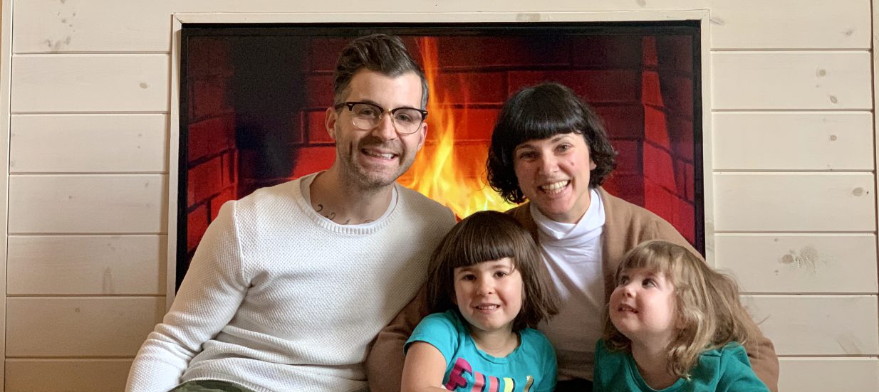 A family of four sits in front of a fireplace.