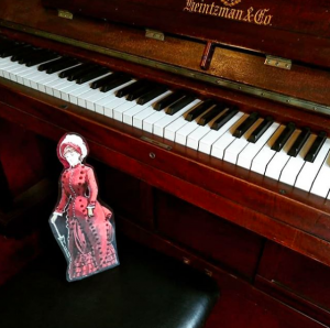 A cardboard cutout of a doll on a piano bench.