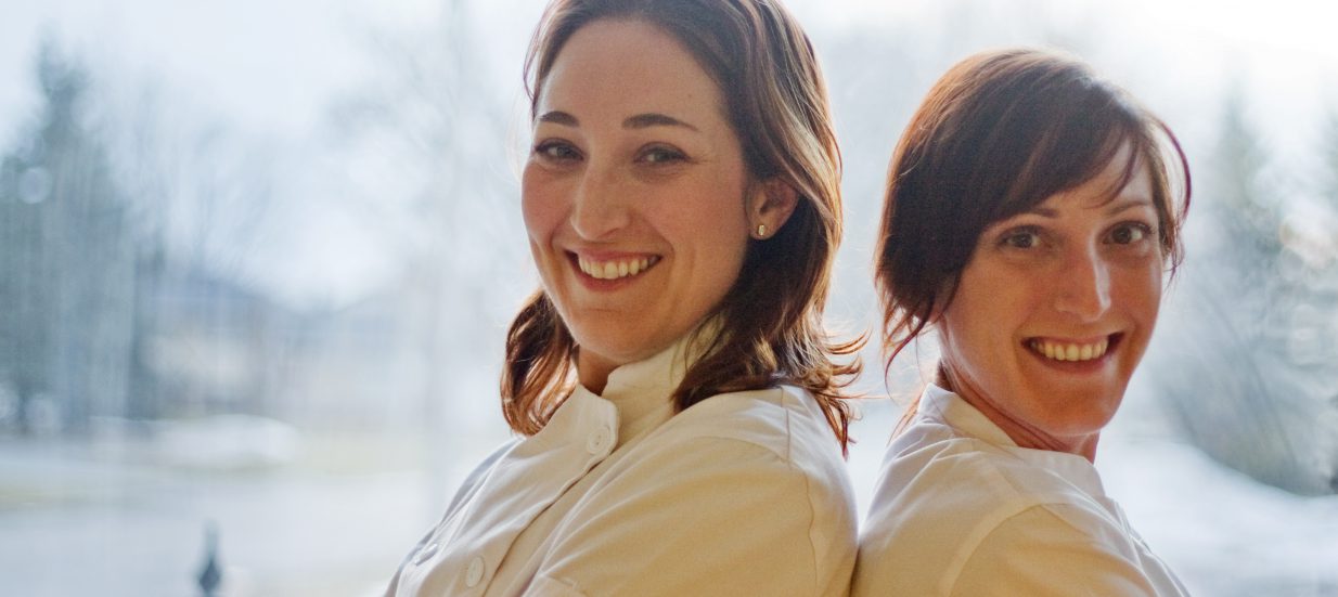 Two women in chef coats standing back to back.