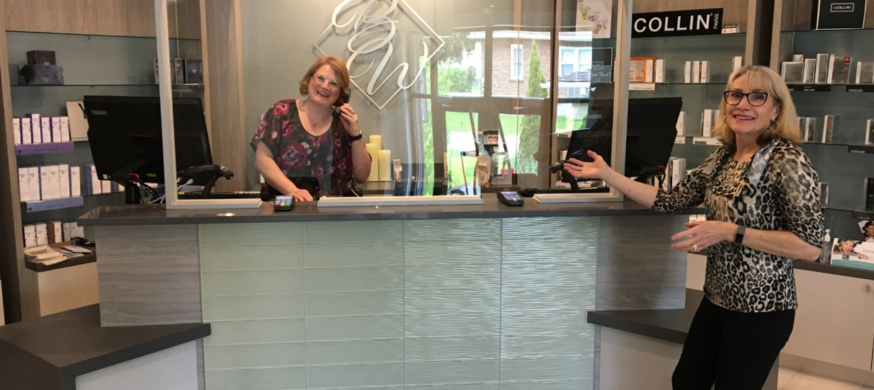 Two women standing at a reception desk with plexiglass.