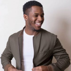 A man in a white shirt and grey jacket smiling and looking to the right.