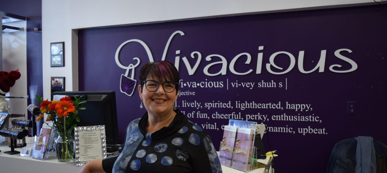 A woman standing in front of a purple sign with the word 'Vivacious' on it.