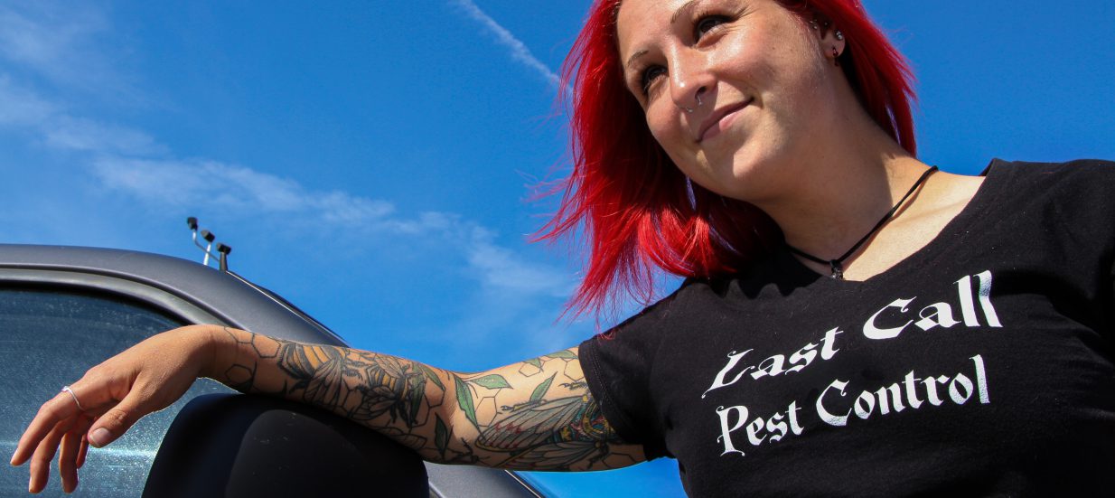 A person with pink hair leaning on a car with blue skies above.