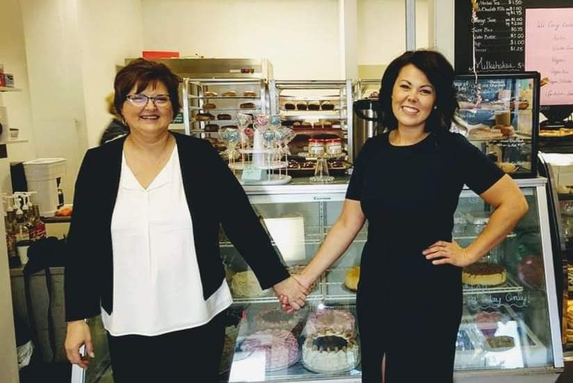 Two women stand side-by-side holding hands.