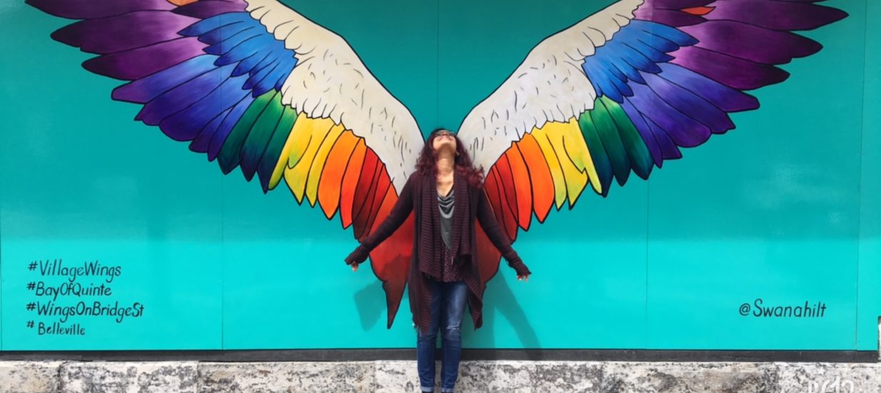 A person standing in front of a turquoise wall with wings painted on the mural.