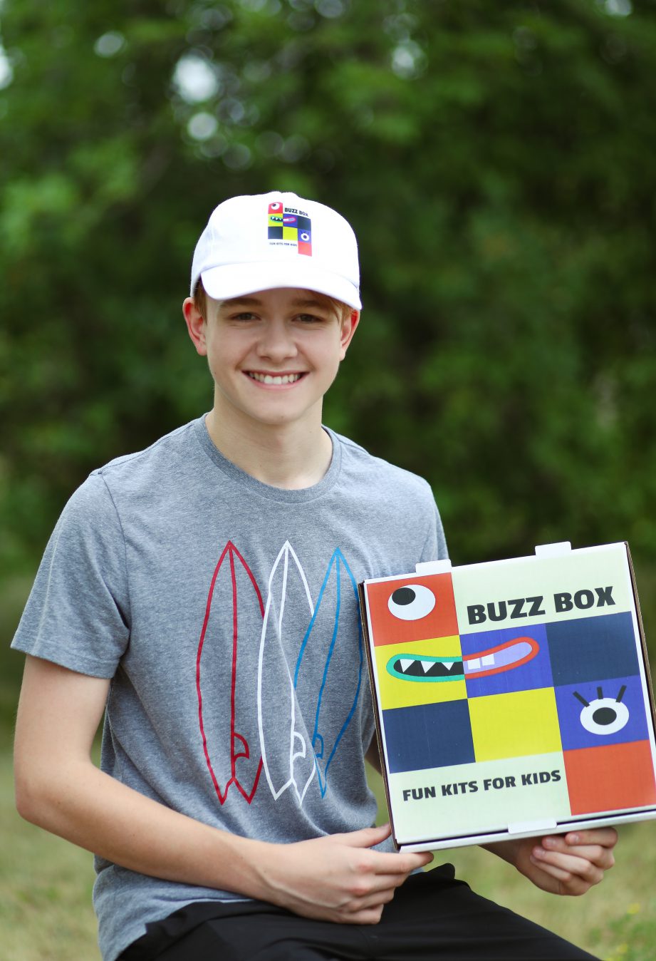 A person standing holding a box that says, "Buzz Box Fun Kits"