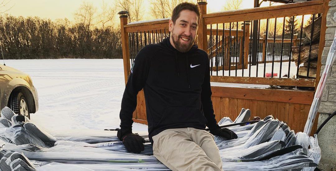 A person sitting on a pile of hockey sticks in the snow. Joey Walsh, owner of HockeyStickMan in Belleville, shares why the Bay of Quinte is a great fit for the business.