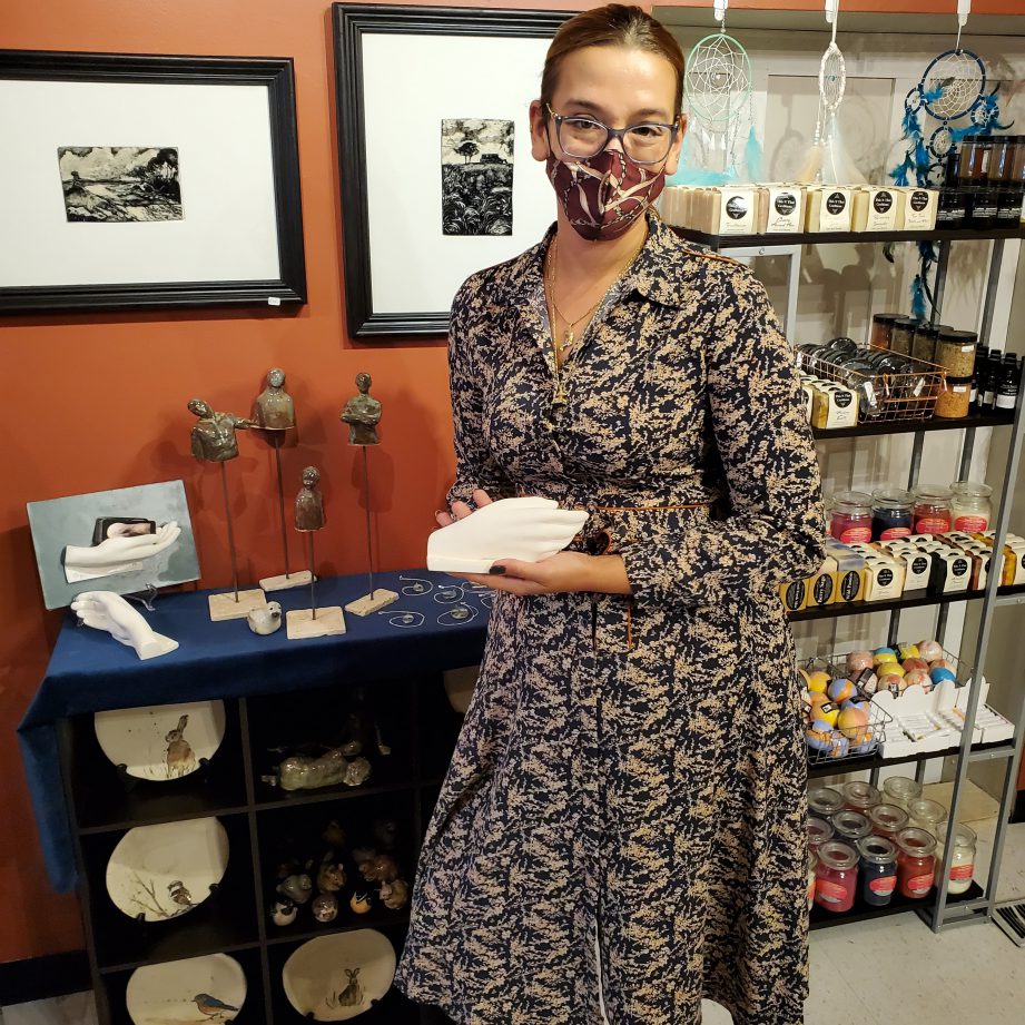 A person wearing a mask standing in front of a wall of art. Kaya Pereira, owner and curator of the Bazaar Artisan Market in downtown Belleville.