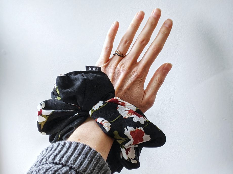 A person's arm extended wearing a black and floral scrunchie.