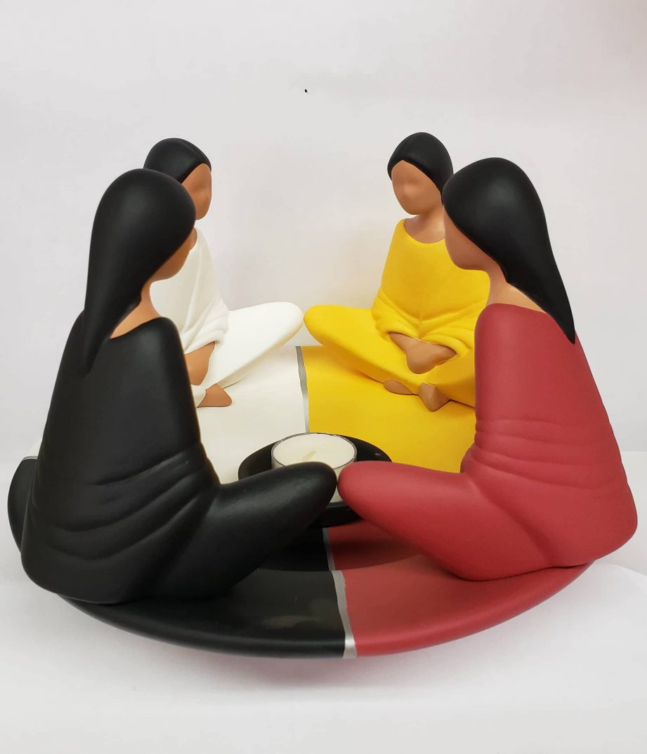 A ceramic candle holder of four women sitting side-by-side in a circle, each wearing a different colour.