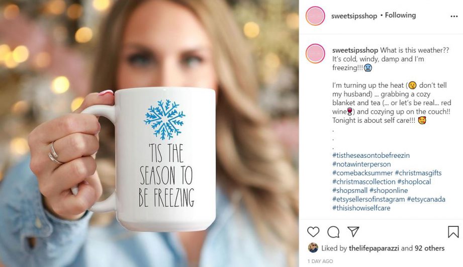 An Instagram account with a photo on the left and caption on the right. The photo is of a person in a blurred background holding a white mug that says: "Tis the season to be freezing."