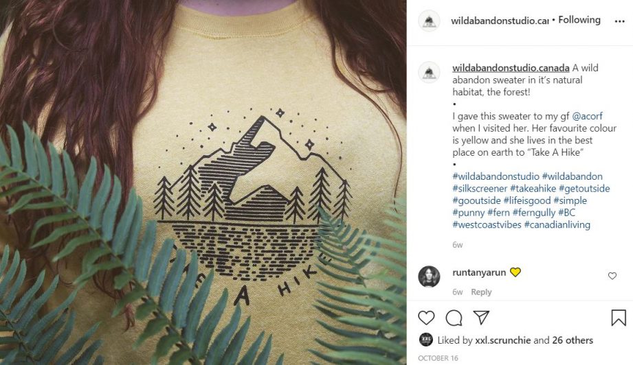 A person wearing a yellow t shirt with an illustration of a mountain with text underneath: 'Take a hike.'