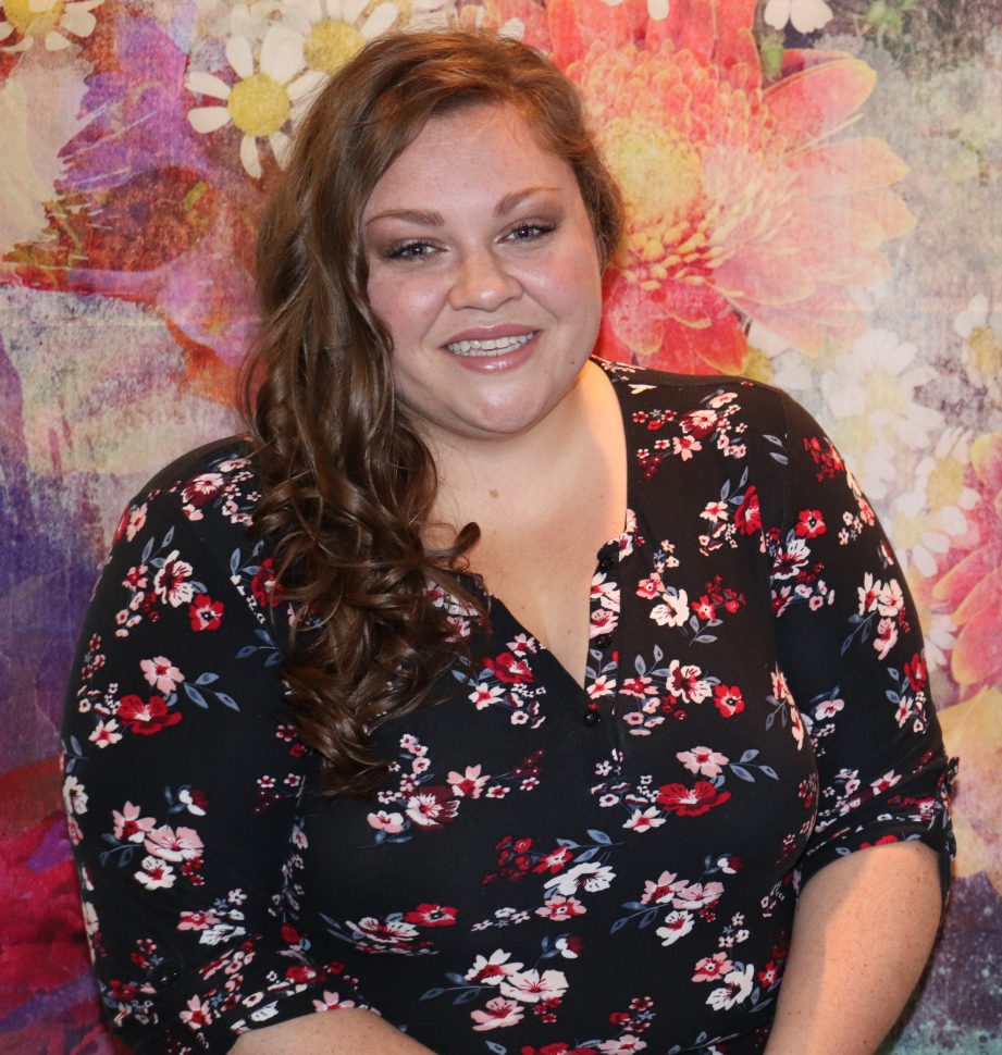 A person wearing a floral top standing in front of a multi-coloured wall.