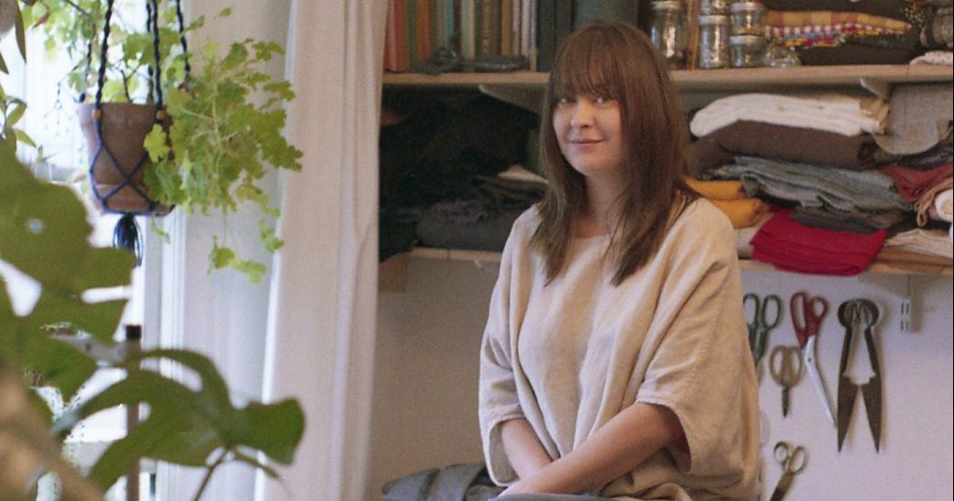 A person sitting in front of a shelf with hanging plants to the left.