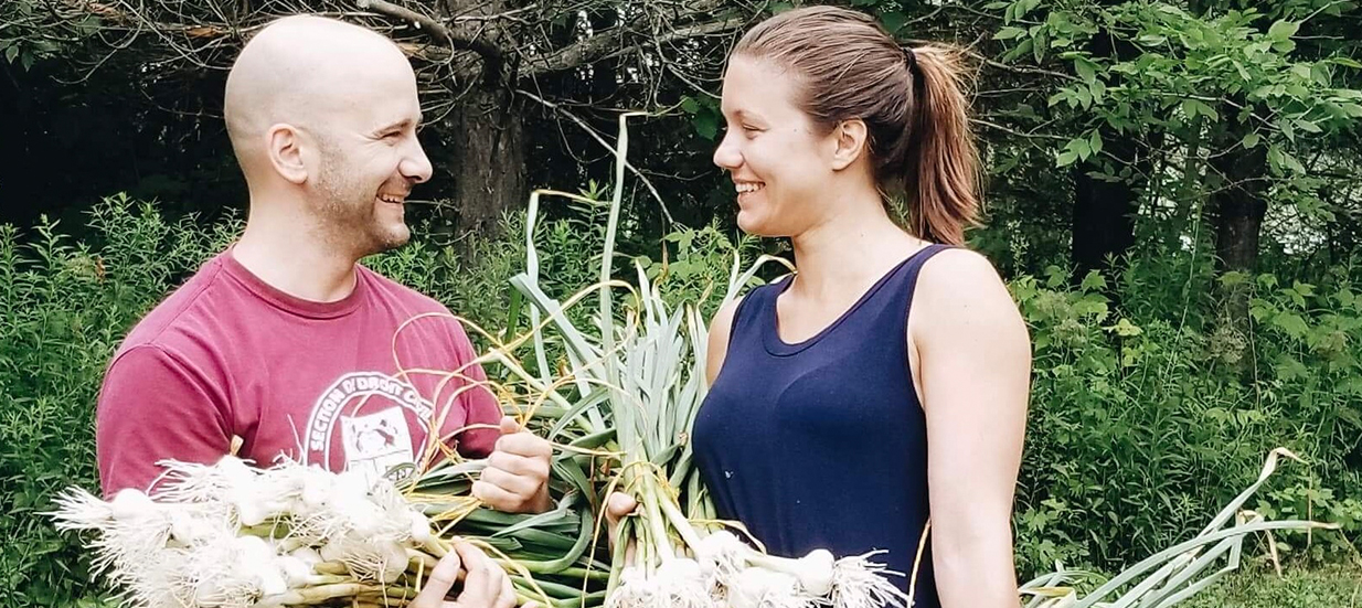 Two people standing facing each other holding bunches of garlic.