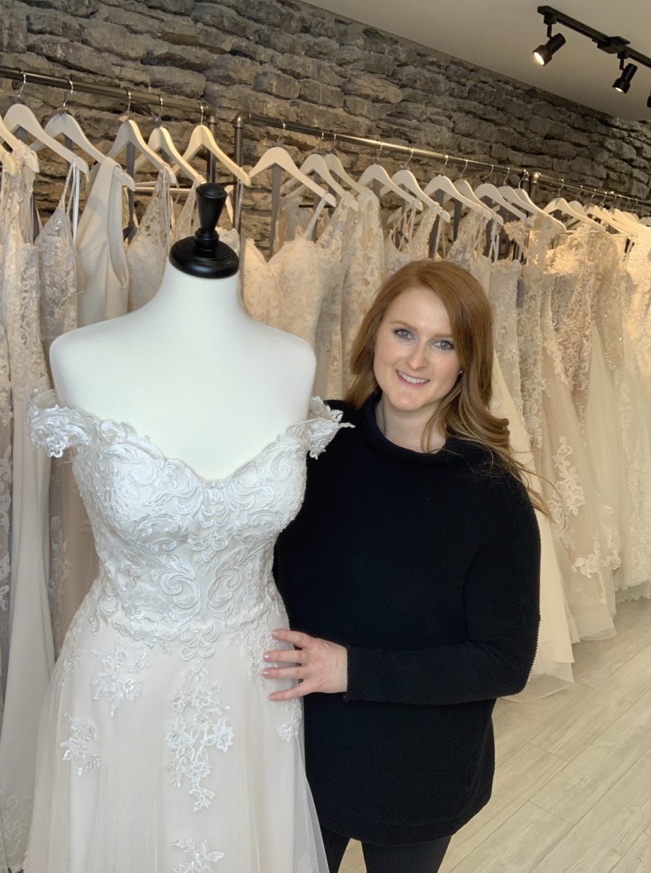 A person standing next to a wedding dress on a mannequin.