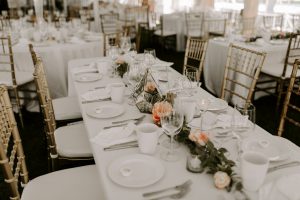 A long table at a wedding with white tablecloth, place settings and flowers.