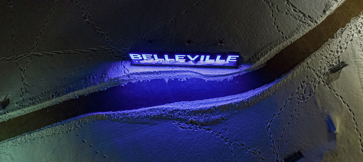 Aerial shot of snowy ground with footprint and a glowing 'Belleville' sign.