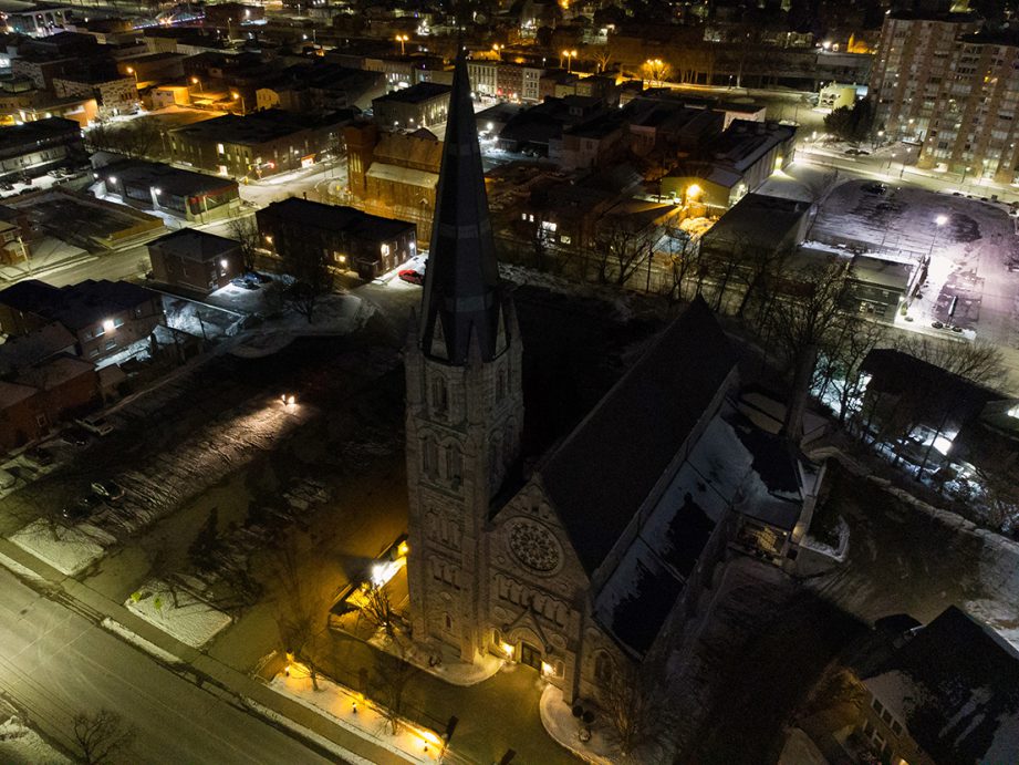 An aerial photo of a church at night with lights and buildings in the background.