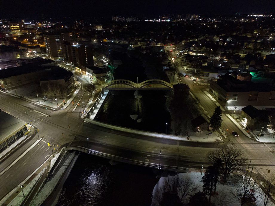 Aerial shot of a river at night with two bridges and city street lights alongside it.