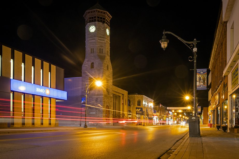 A streetscape at night with a large clocktower and light streaks from cars.