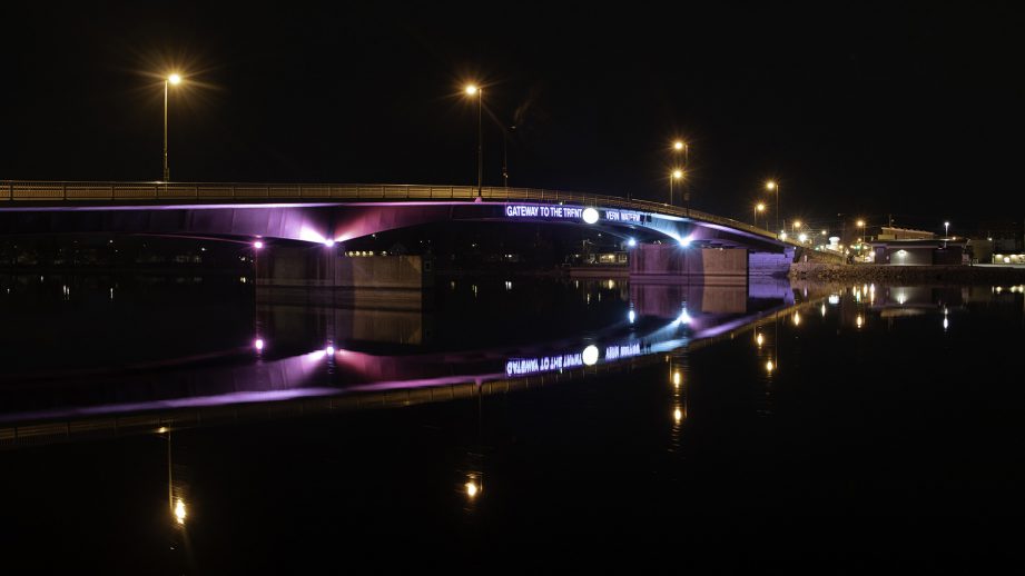 A bridge at night with lights reflected in the water below.