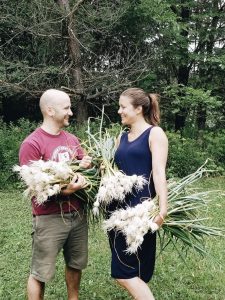 Two people standing facing each other holding bunches of garlic.