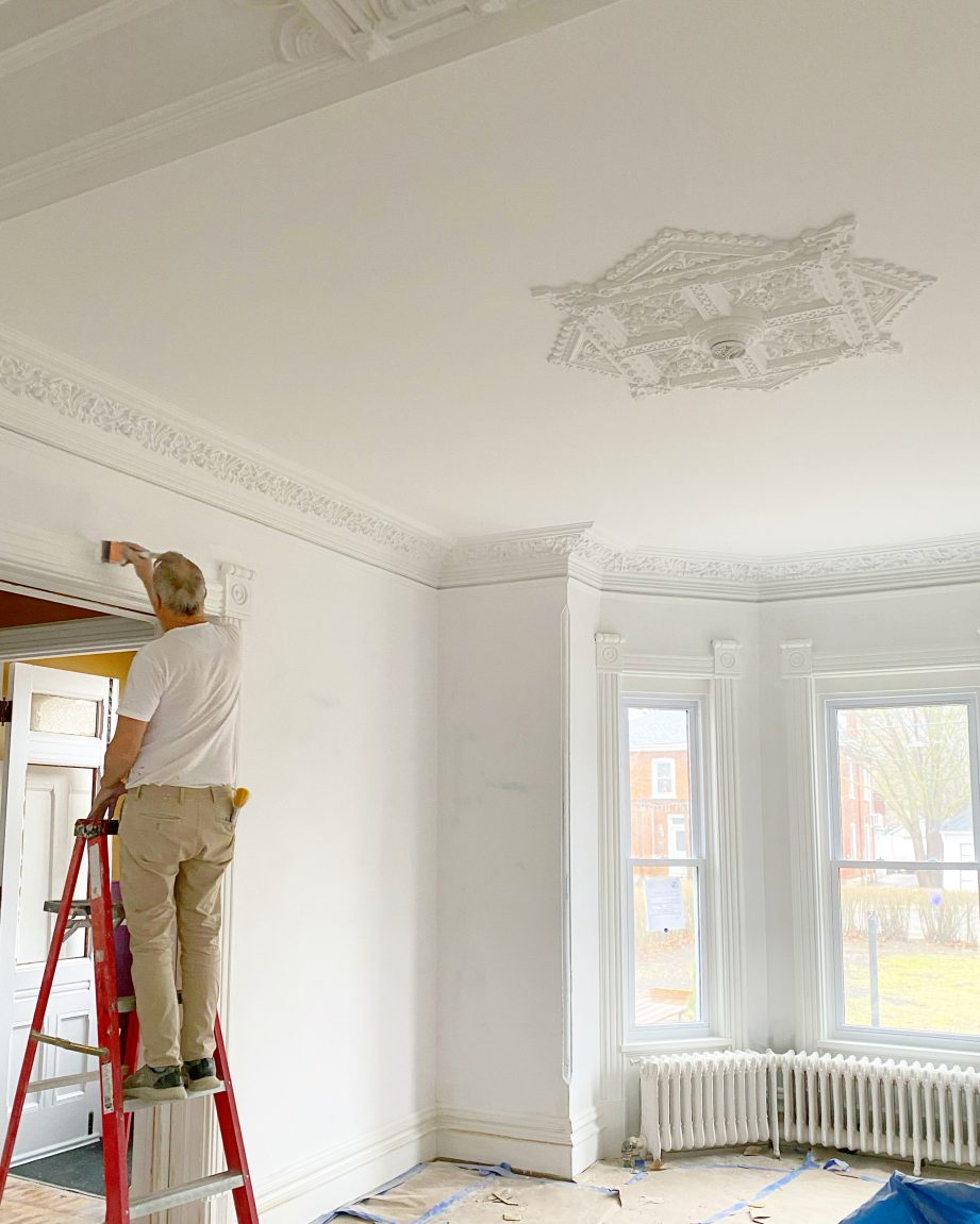 A person on a ladder painting a white room.