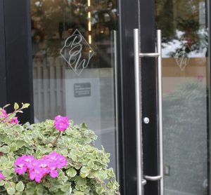 A black door with silver handle and flowers out front.