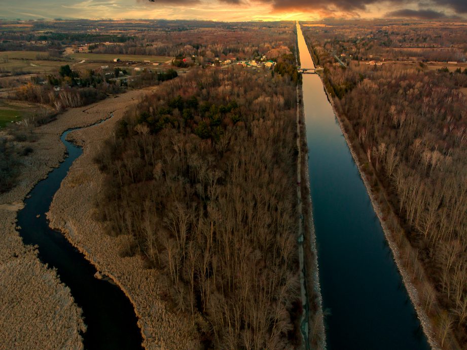 An aerial photo of a canal surrounded by trees and countryside at sunrise.