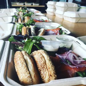 A row of takeout containers with bagels, vegetables and greens.