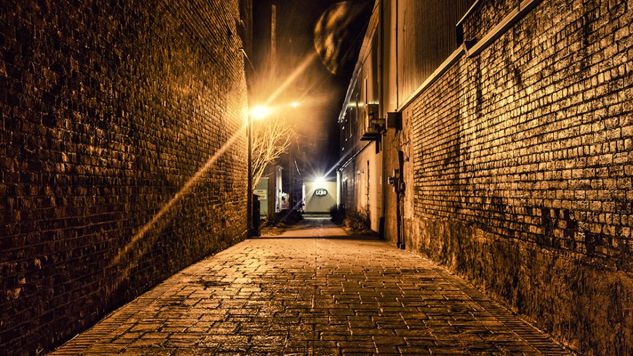 An alley at night, with golden light shining on the walls and footpath.