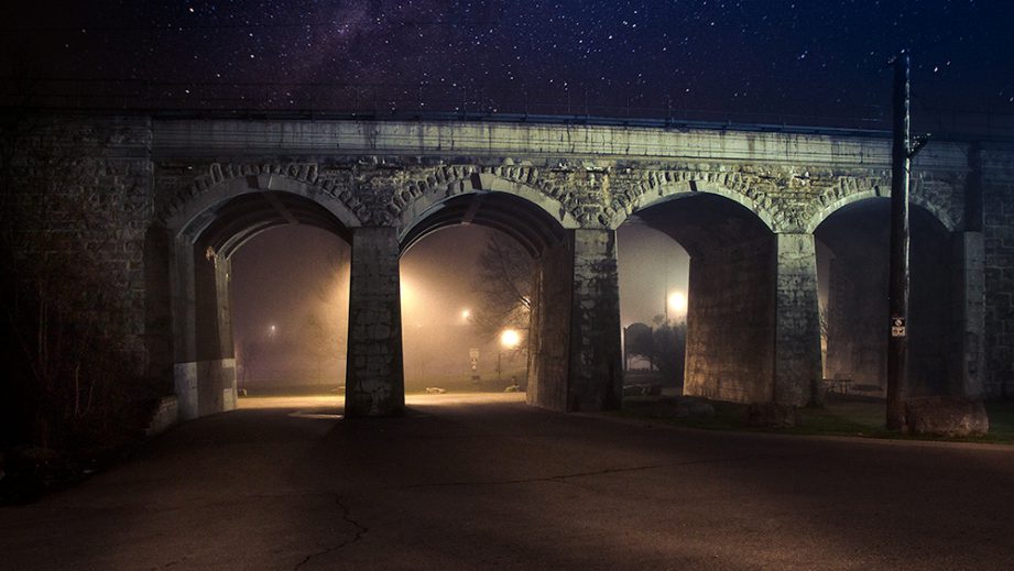 A stone bridge with arches at night, with a starry sky in the background.