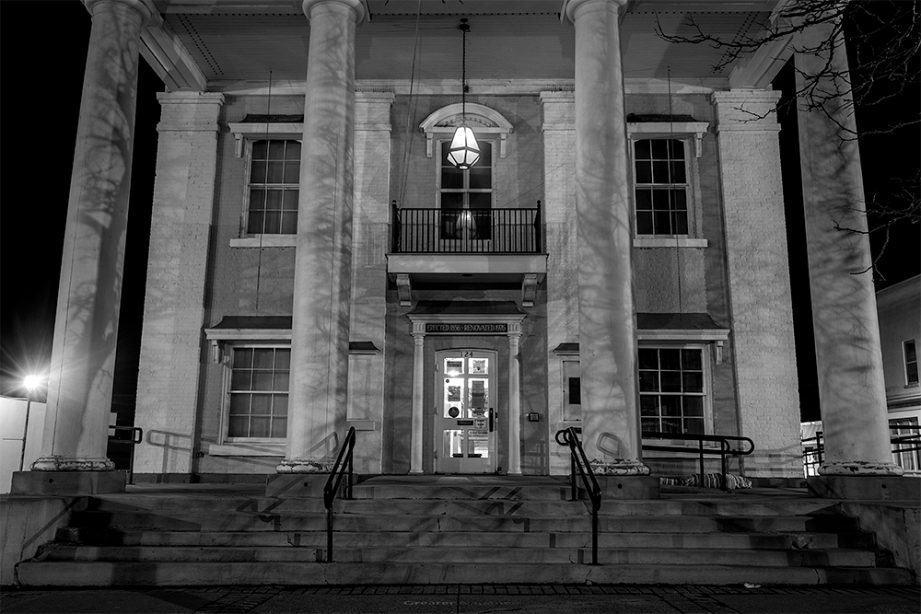 A black and white photo of a white building, Napanee Town Hall, with tall pillars and the front steps leading to the building.