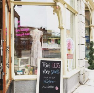 A storefront with a chalkboard sign and a dress in the window.