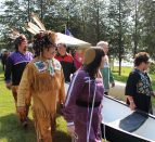 a group of Mohawk people dressed in regalia holding a canoe and walking on grass towards the water for the Mohawk Landing celebration.