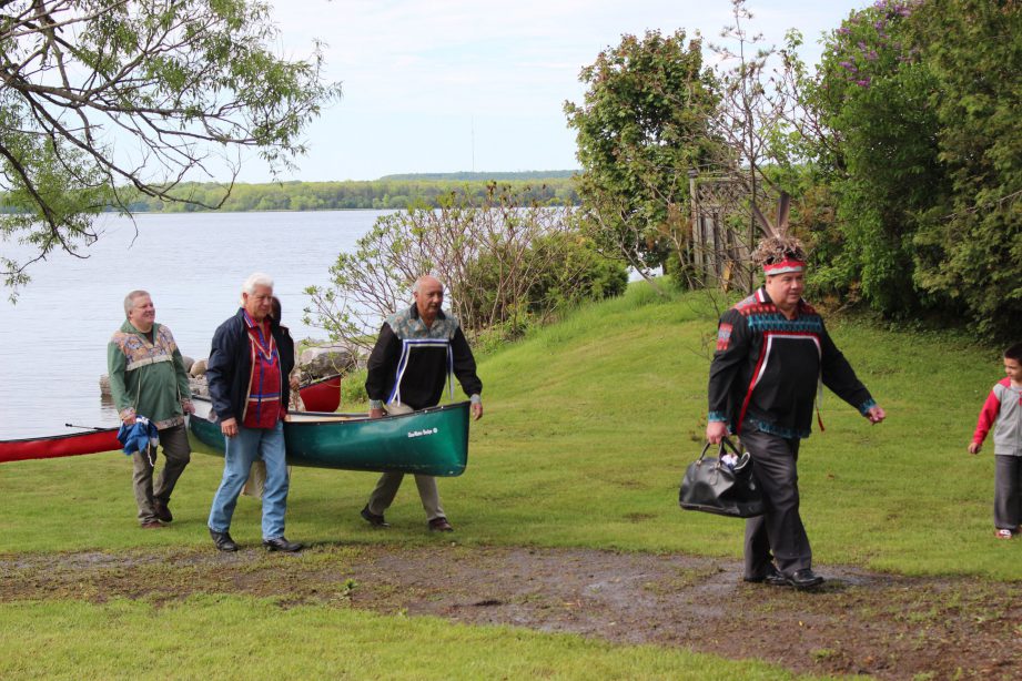 Mohawk people holding a canoe and walking on grass away from the water for the Mohawk Landing celebration.