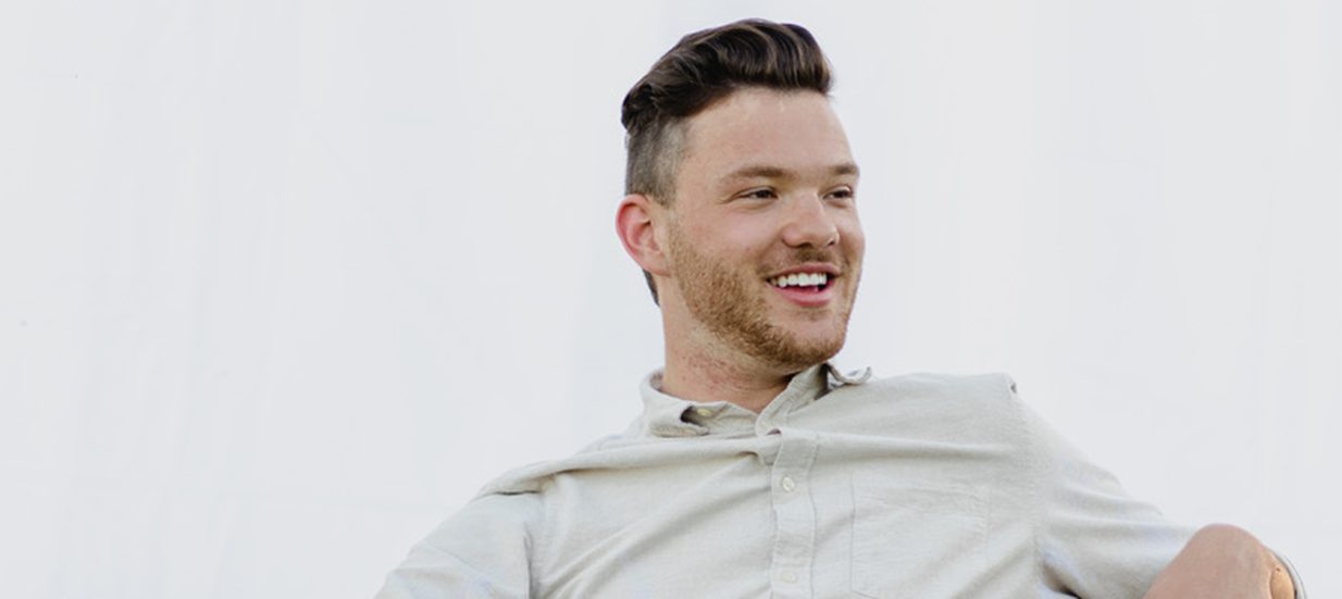 A person wearing a white button down shirt, looking away from the camera, sitting in front of a white backdrop.