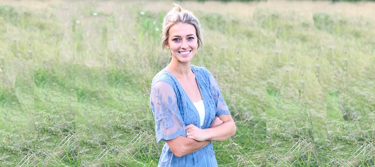 A person smiling, standing with their arms crossed in a grassy field. Meet Jennifer Oram, the entrepreneur behind Songbird Reflexology in Quinte West.