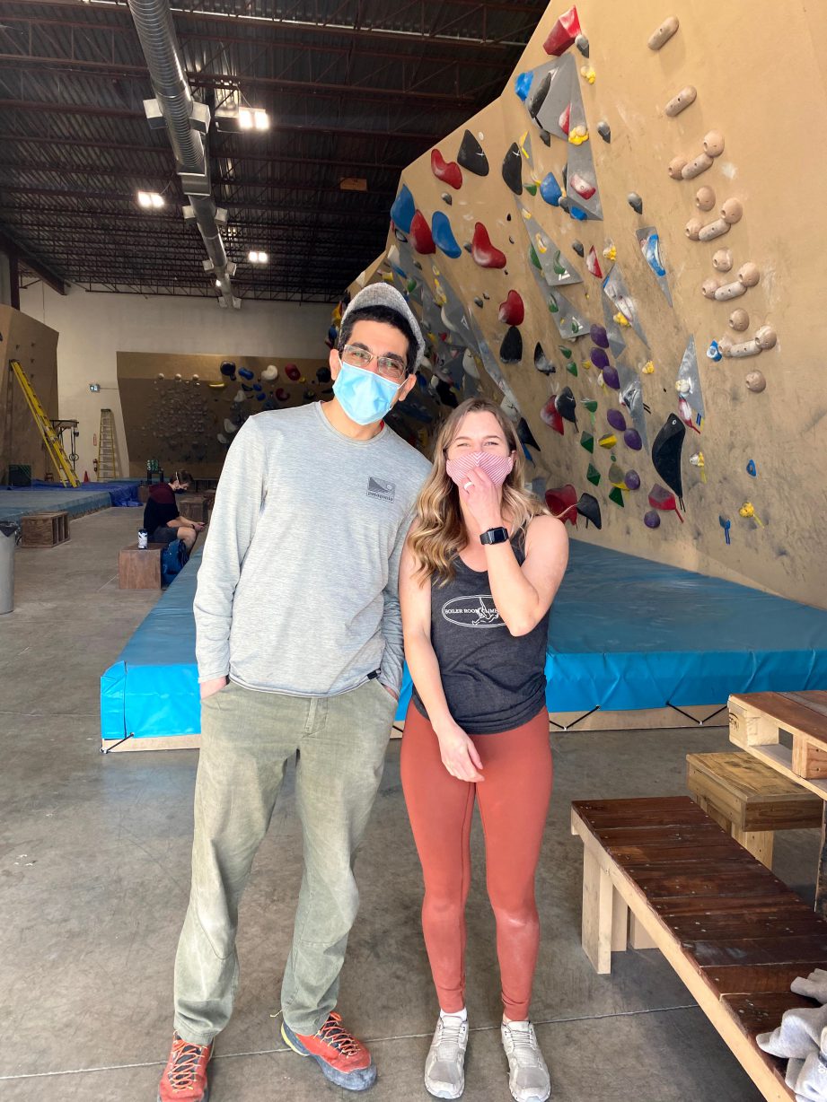 Two people wearing masks standing next to each other in a climbing gym.