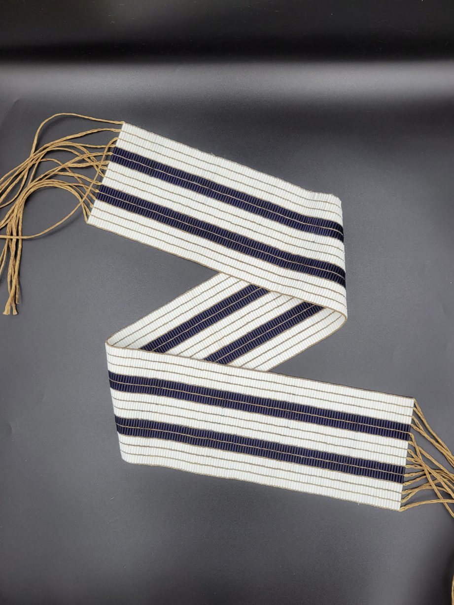 A two row wampum belt, made of white and purple beads, folded in half.