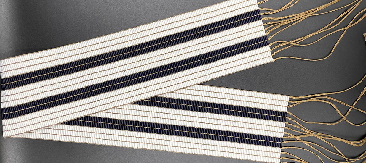 A two row wampum belt, made of white and purple beads, folded in half.