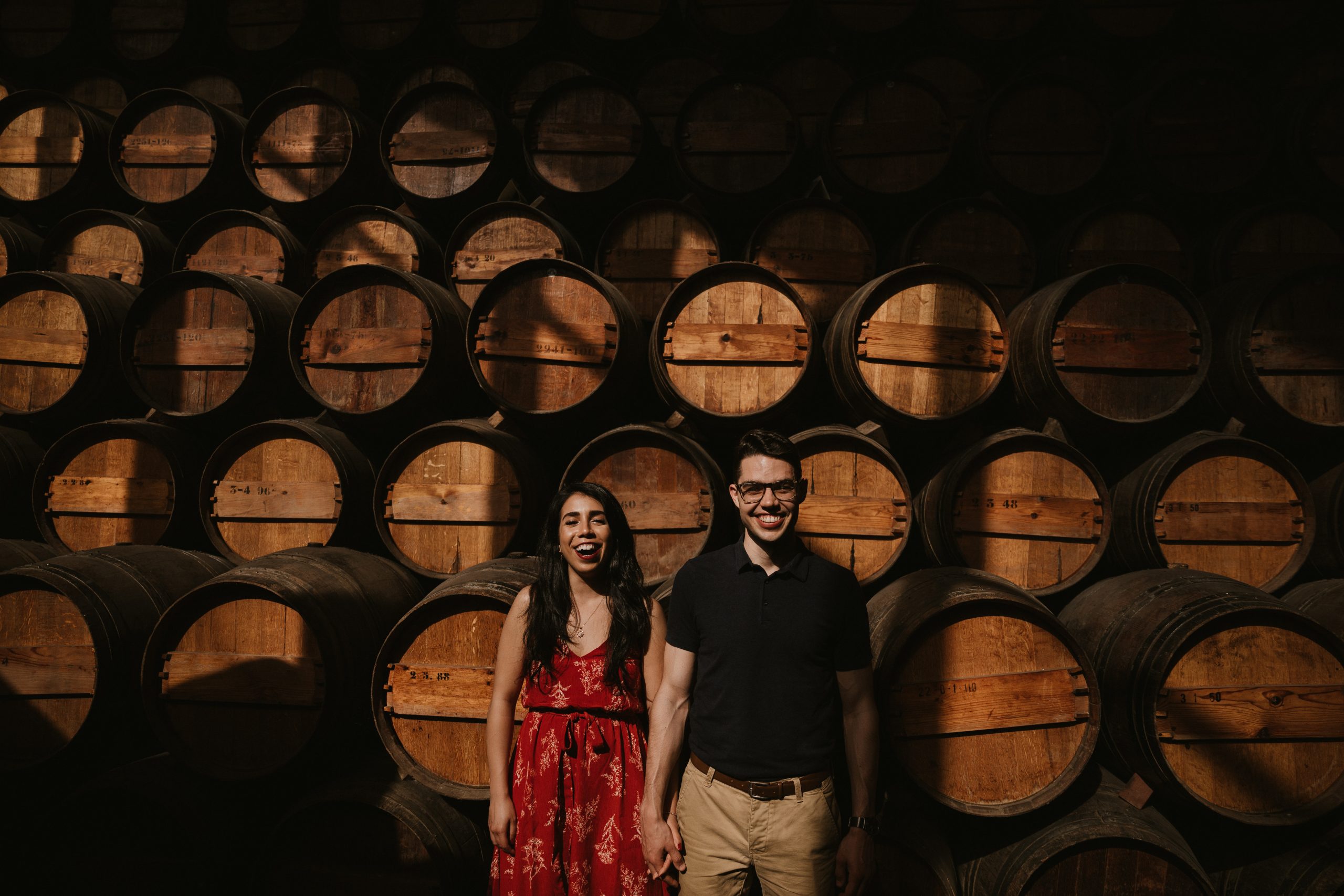 Alex and Meghan Callisto, owners of The Cottage by Callisto, standing side-by-side holding hands with wine barrels in the background.