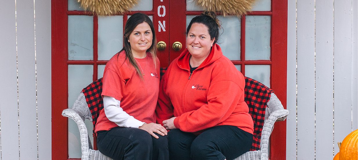 Two staff from Cheer Farms wearing red shirts and black pants, sitting on a bench in front of a red door.