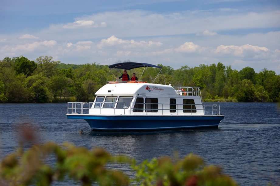 A houesboat from H2O Getaways on the water with trees in the background.