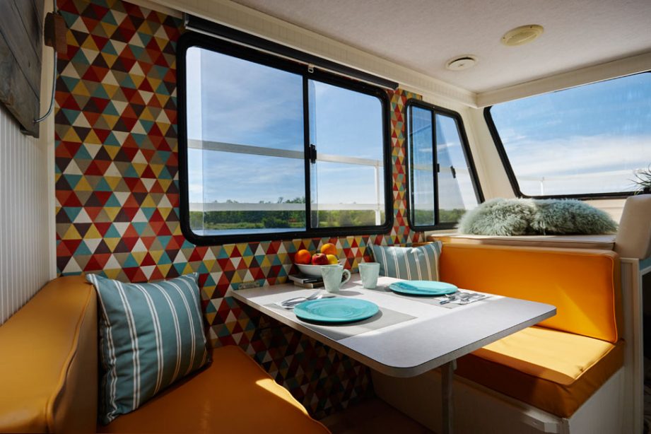 Interior of a houseboat from H2O Getaways; a dining area with two orange benches and retro wallpaper.