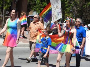 People marching in the Bay of Quinte Pride parade wearing rainbow dresses and waving Pride flags.